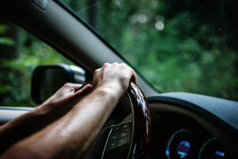 Close-up of a person's hands gripping a wooden steering wheel inside a car.