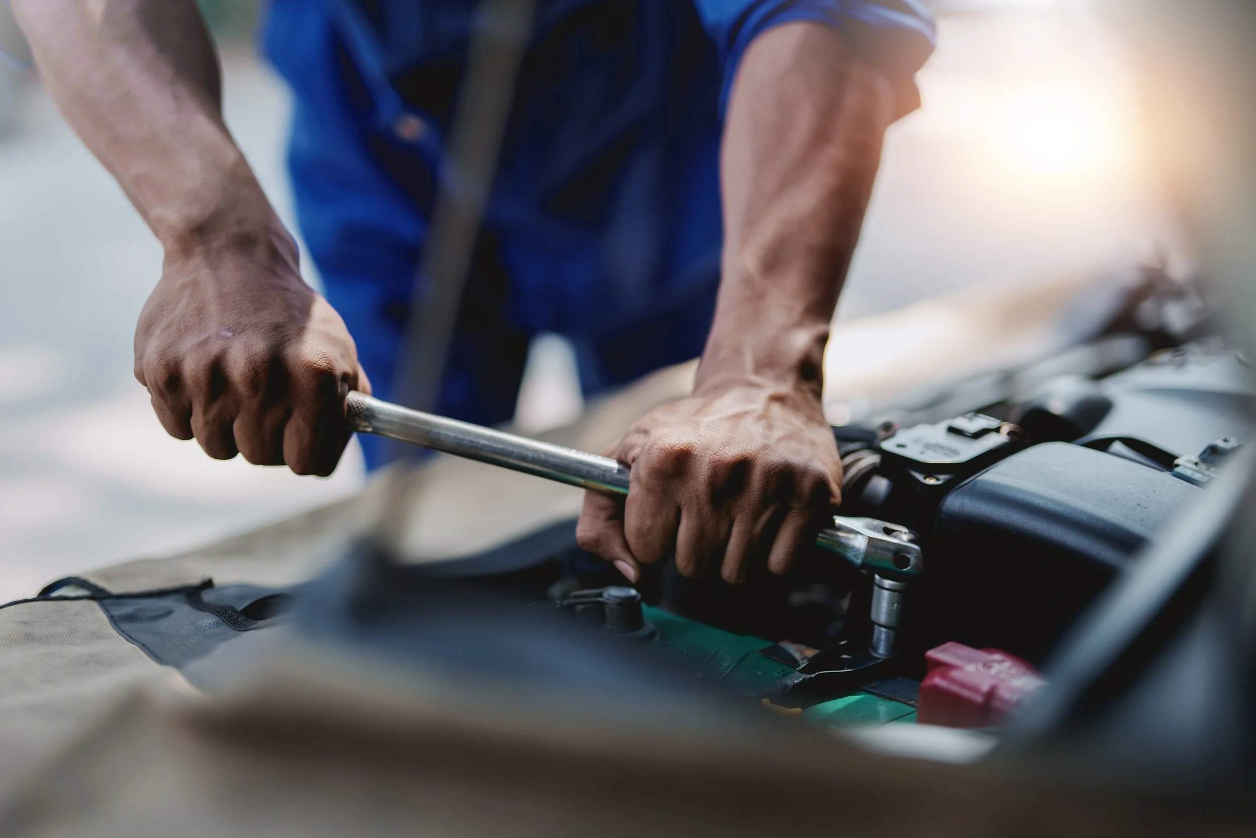 Close-up of a mechanic's hands tightening a bolt on a car engine with a wrench.