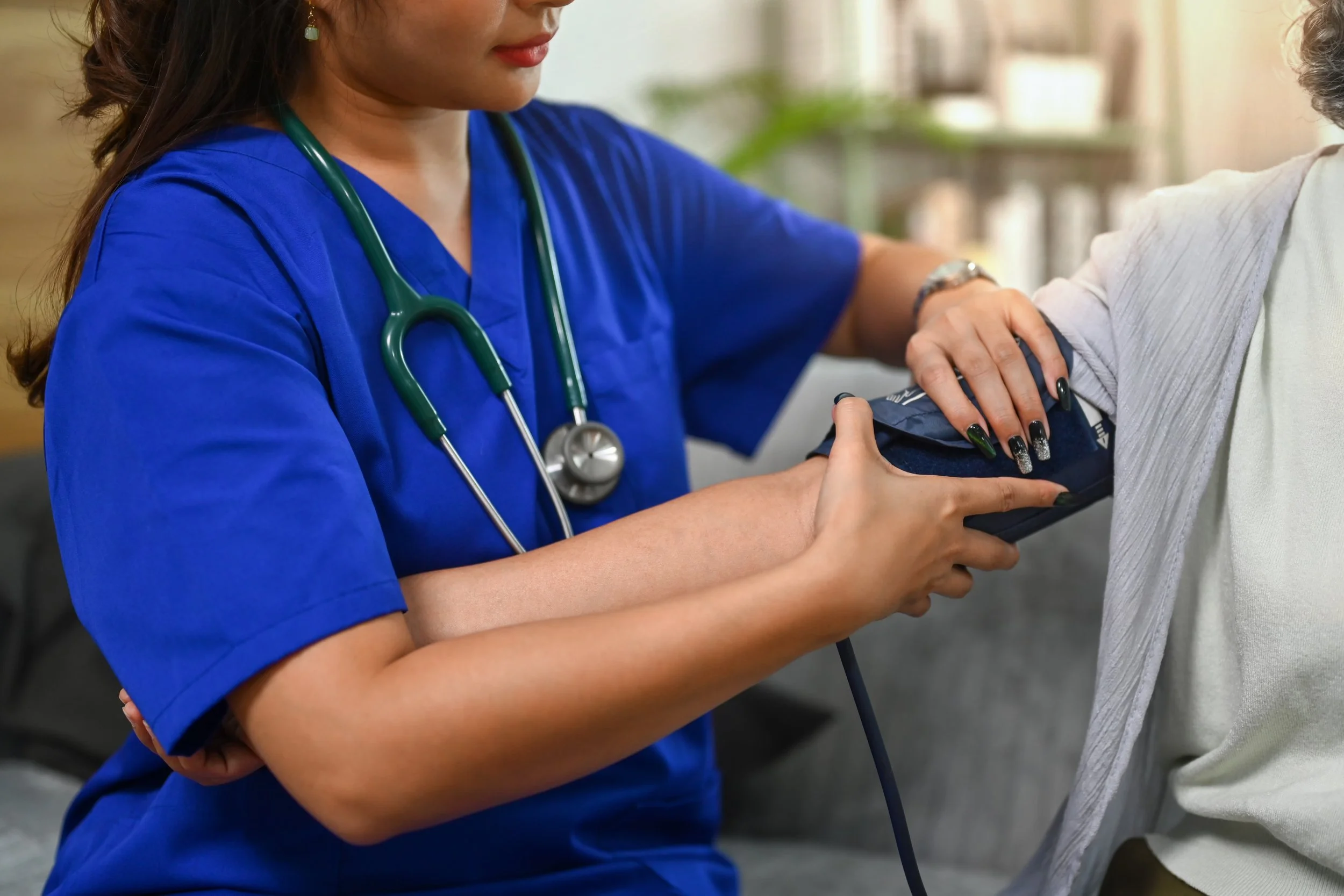 Healthcare professional in blue scrubs measuring patient's blood pressure with cuff.