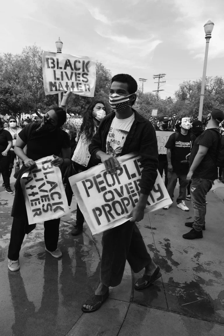 Black and white image of masked protesters holding signs reading "Black Lives Matter" and "People Over Property.
