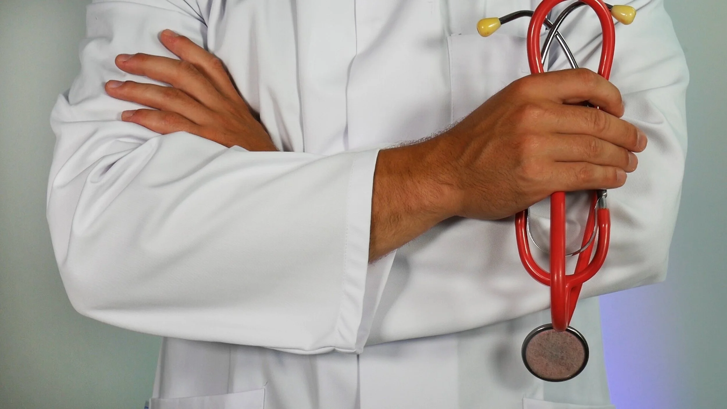 Close-up of a person in a white lab coat holding a red stethoscope.
