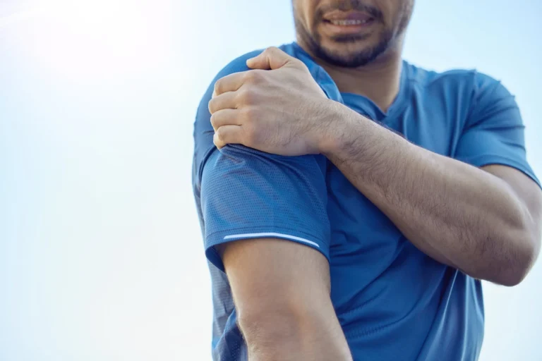 Man in blue athletic shirt holding his right shoulder with a pained expression.