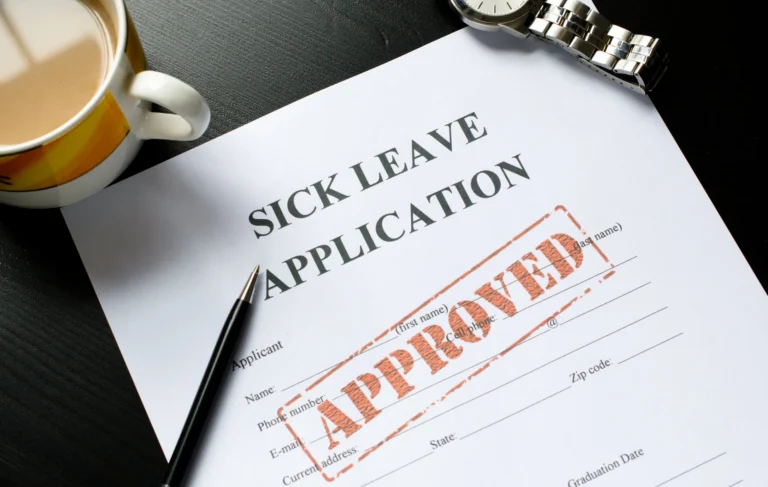 Sick leave application form with "APPROVED" stamp, black pen, wristwatch, and coffee cup.