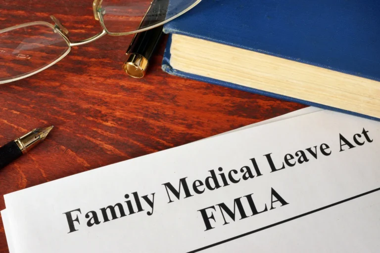 Close-up of a Family Medical Leave Act (FMLA) document on a wooden desk with glasses, a fountain pen, and a blue hardcover book.