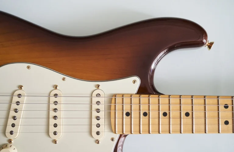 Close-up of a sunburst electric guitar body and maple neck with six strings and white pickguard.