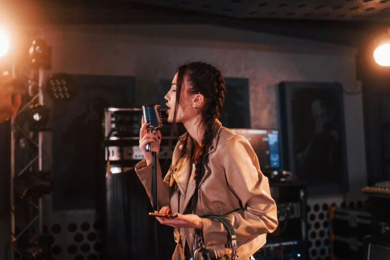 Young woman with braided hair singing into a vintage microphone in recording studio.