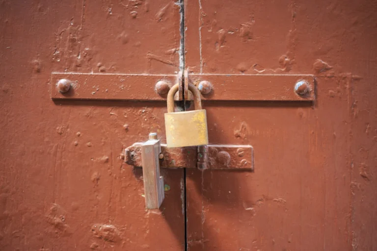 Close-up of a rusty padlock securing a weathered brown metal door latch.