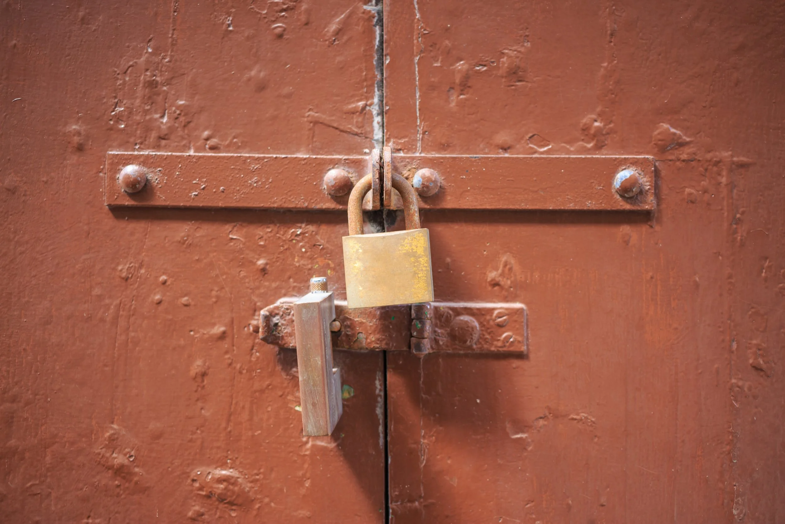 Close-up of a rusty padlock securing a weathered brown metal door latch.