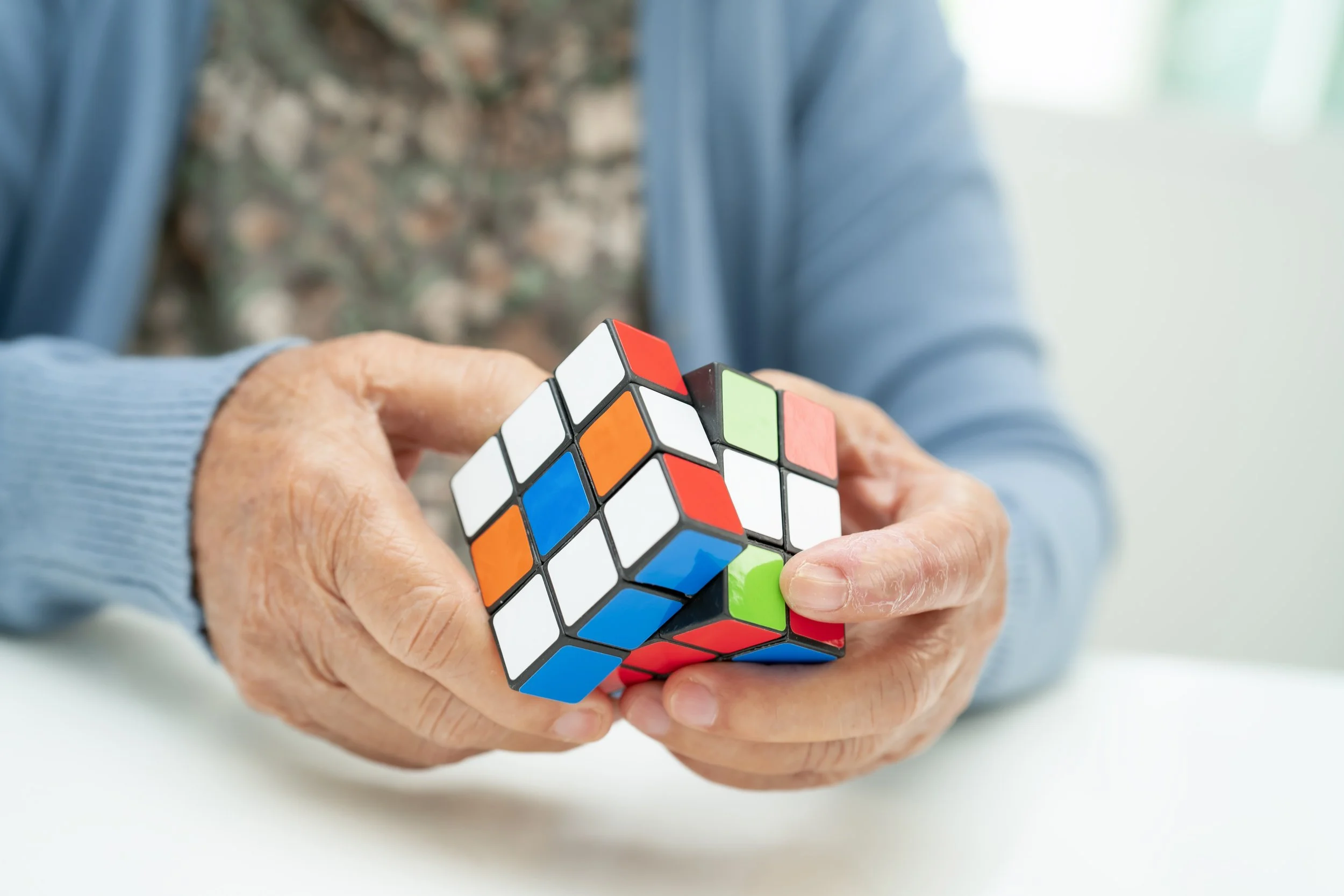 Close-up of elderly hands manipulating a partially solved Rubik's Cube with colorful stickers.
