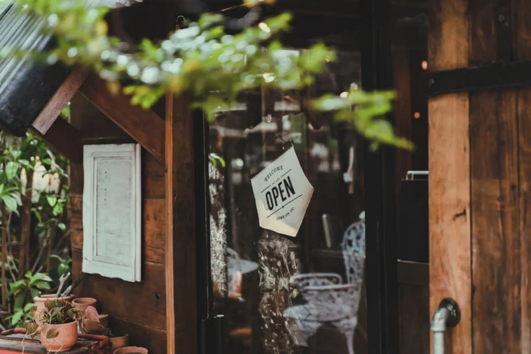 Glass door with a hanging "Welcome, We Are Open" sign on a rustic wooden building.