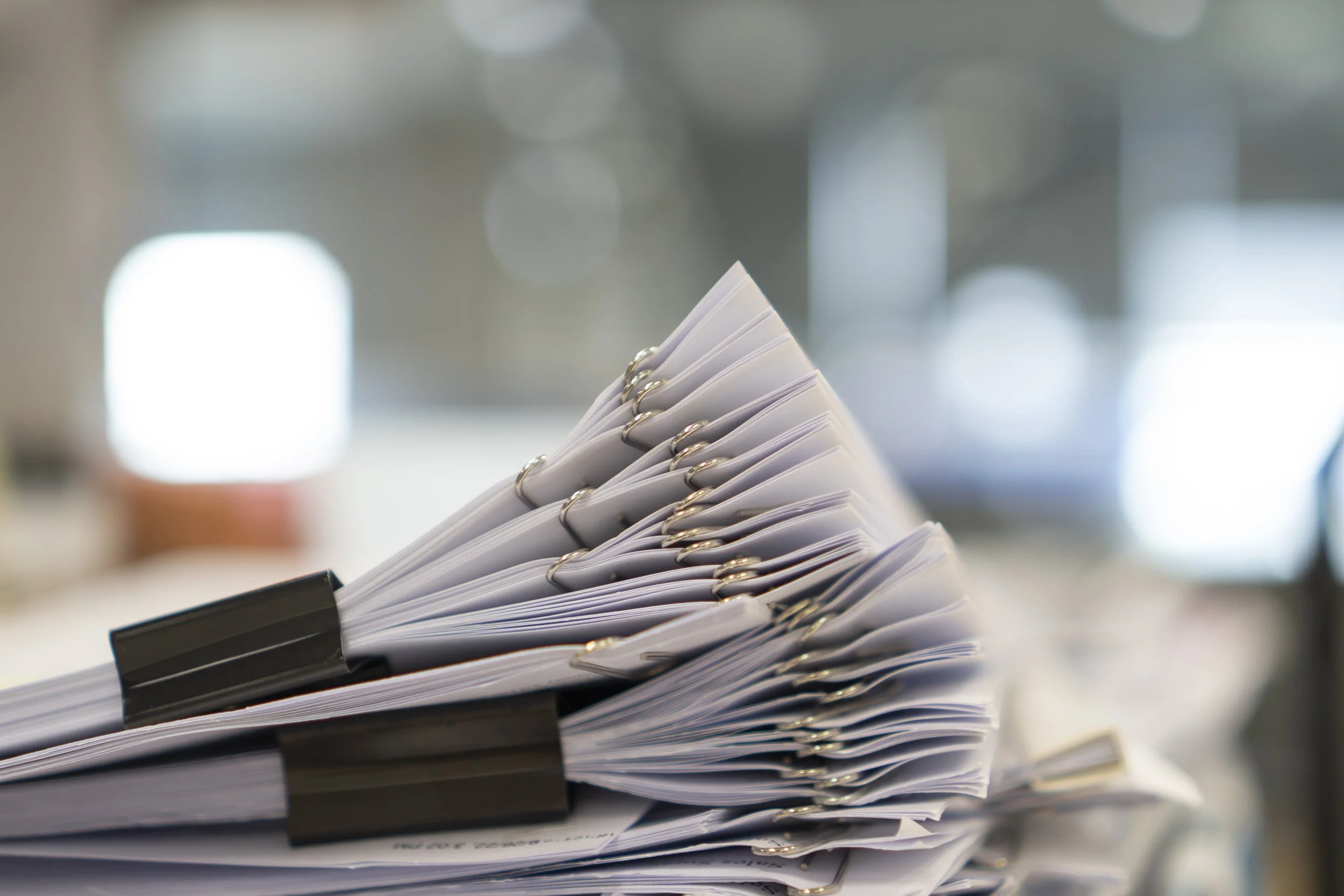 Stack of white papers organized with black binder clips on a blurred background.