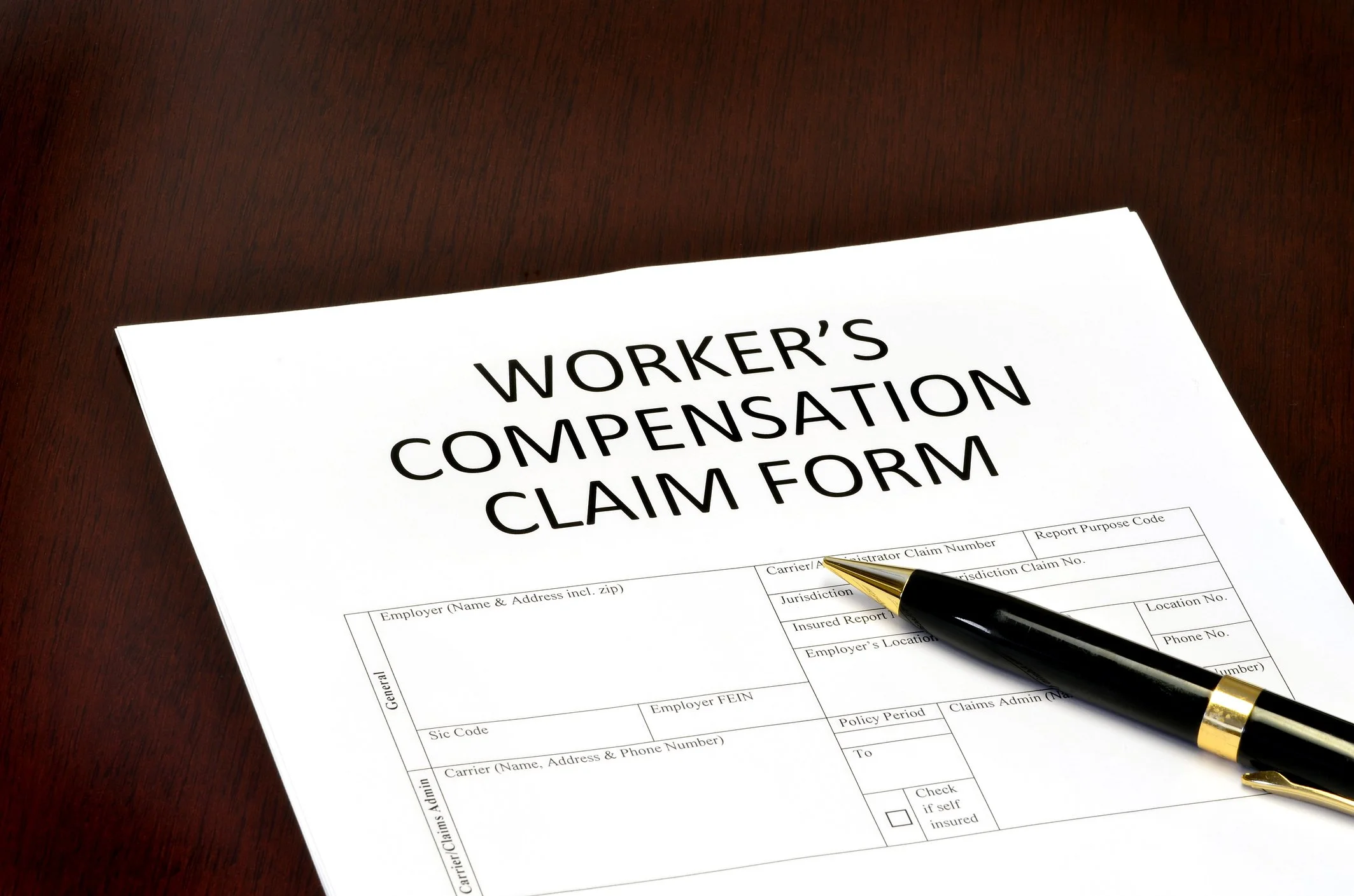Worker's Compensation Claim Form on wooden desk with black and gold pen.