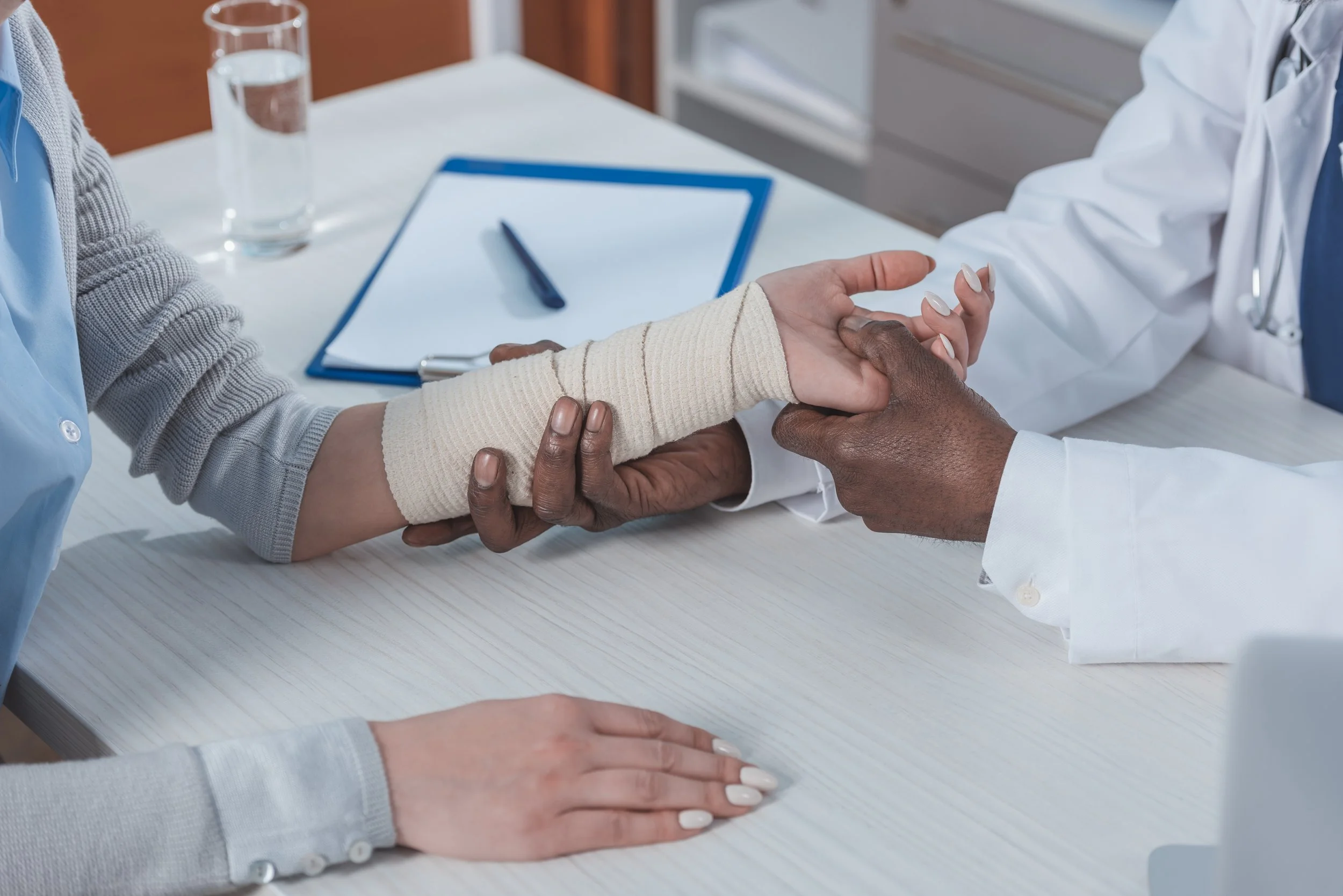 Doctor examining patient's bandaged forearm during medical consultation at desk.
