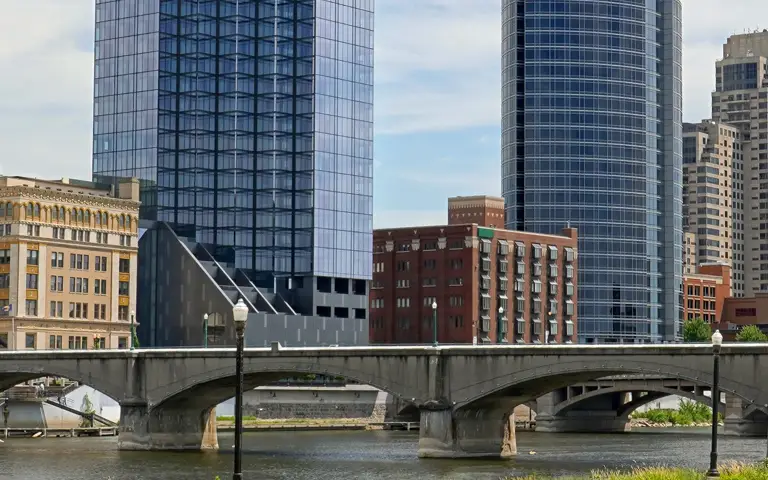 Urban river scene with concrete bridge, modern glass skyscrapers, and historic brick buildings.