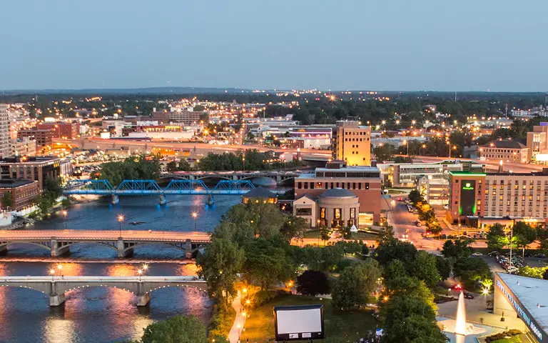 Aerial view of a cityscape at dusk with illuminated bridges and buildings along a river.
