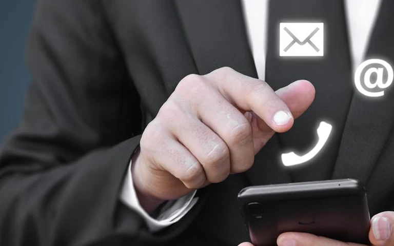 Businessperson in black suit interacting with smartphone, icons of email, phone, and at symbol floating.